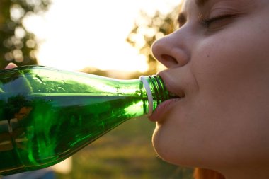Doğadaki neşeli kadın ferahlatıcı bir içecekten su içiyor.