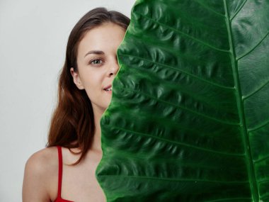 Güzel bir kadın yüzünün yarısını büyük yeşil bir yaprak kaplama stüdyosuyla kapatıyor.