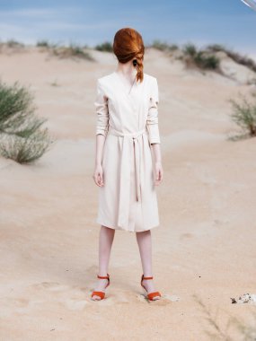 Kumsaldaki ceketli kızıl saçlı kadın poz veriyor.