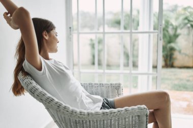 Mutlu kadın pencerenin yanındaki sandalyeye oturur ve doğaya bakar.