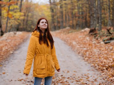 Sarı ceketli kadın sonbahar ormanında yürür. Temiz hava.