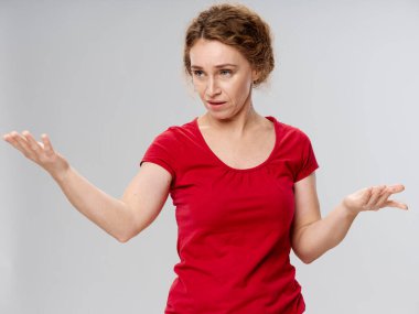 Kırmızı tişörtlü yaşlı kadın, elleri gri arka planda.