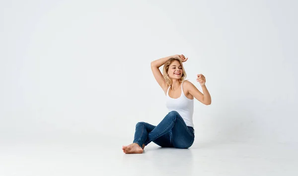 Donna in jeans seduta sul pavimento divertimento emozioni studio isolato sfondo — Foto Stock