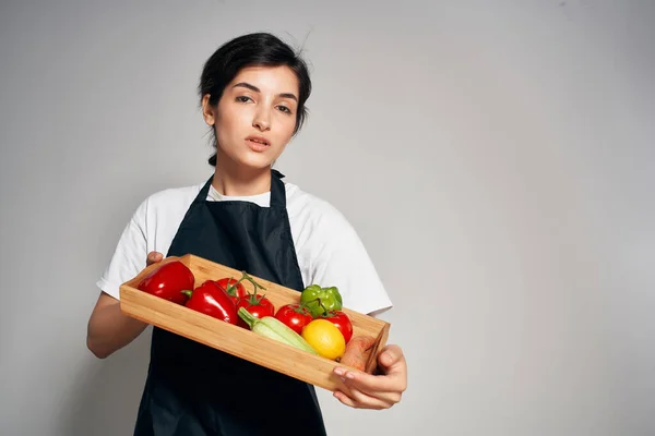 Mujer en un delantal negro una bandeja con verduras comida saludable quehaceres domésticos — Foto de Stock