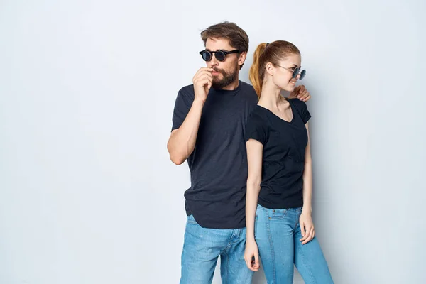 Una giovane coppia in nero t-shirt occhiali da sole posa sfondo chiaro — Foto Stock