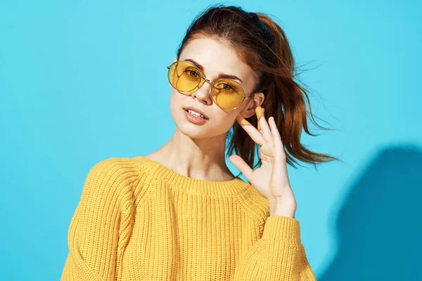 Woman in yellow sweater holding her hair studio posing blue background — Stock Photo, Image