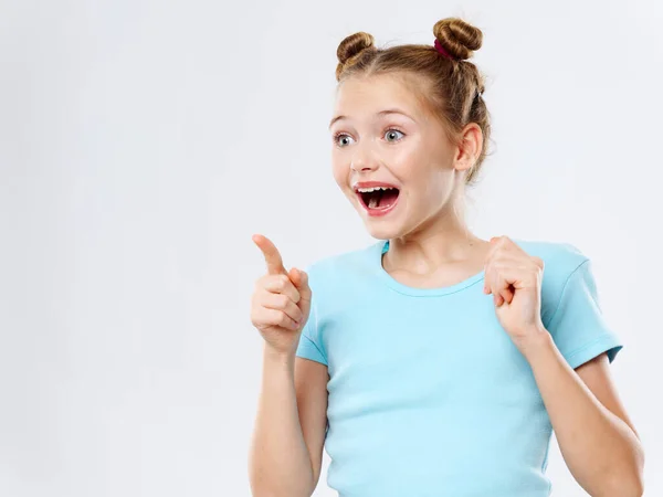 Gelukkig meisje in een t-shirt met een kapsel wijst haar vinger naar de zijkant en lacht — Stockfoto