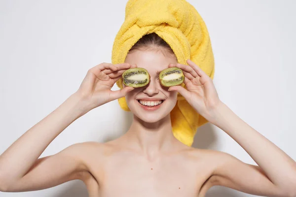Wanita dengan bahu telanjang dengan handuk kuning di kepalanya kiwi di tangannya kulit bersih — Stok Foto