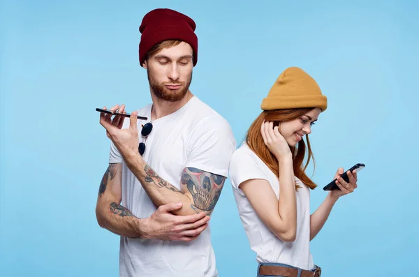 Jovem casal em chapéus com telefones em mãos comunicação de moda — Fotografia de Stock