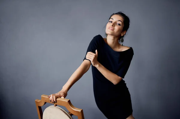 Mulher bonita em um vestido preto perto da cadeira estúdio de estilo de vida de moda de luxo — Fotografia de Stock
