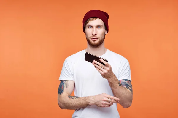 Man in een wit t-shirt met een telefoon in zijn handen in communicatie technologie oranje achtergrond — Stockfoto