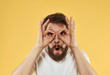 Sarı arka plandaki neşeli sakallı adam elleriyle el kol hareketi yapıyor.