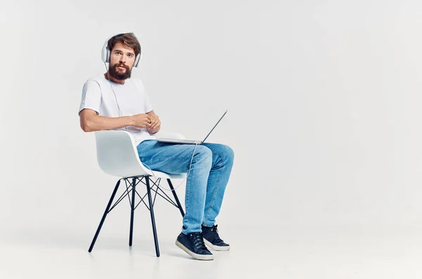 Homme en t-shirt blanc assis sur une chaise avec un ordinateur portable dans le divertissement casque — Photo