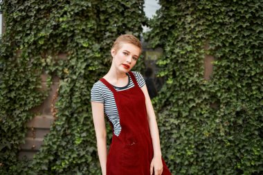 Kısa saçlı kadın yeşil çalılık pozu veriyor.