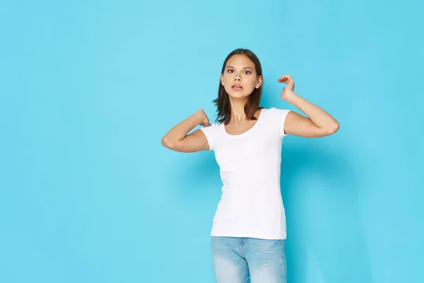 Giovane donna in jeans in una t-shirt gesti con le mani su uno sfondo blu Copia Spazio — Foto Stock