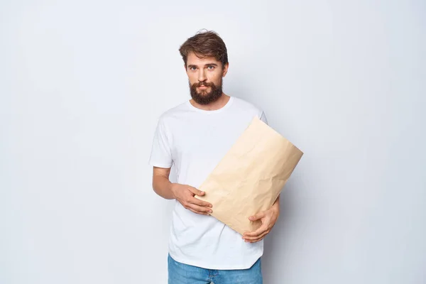 Hombre alegre en camiseta blanca con bolsa de papel embalaje fondo claro — Foto de Stock