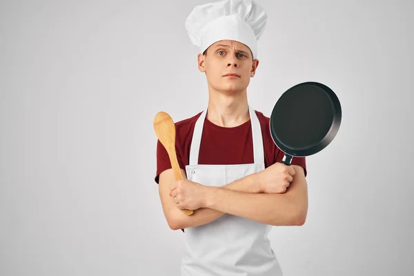 Un uomo in grembiule bianco una padella tra le mani preparare il cibo per i professionisti sfondo leggero — Foto Stock