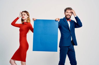 Takım elbiseli adam, kırmızı elbiseli kadının yanında mavi mokasen posterli adam.