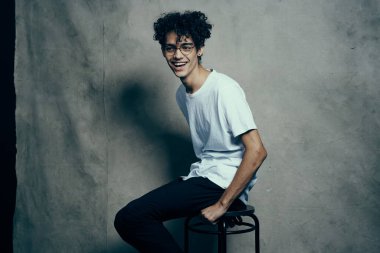 Sandalyede oturup poz veren kıvırcık saçlı sevimli adam.