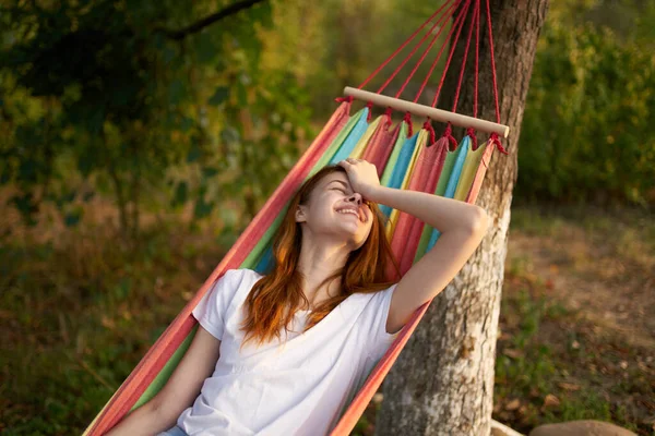 Glad kvinna i en vit t-shirt ligger i en hängmatta utomhus natur — Stockfoto