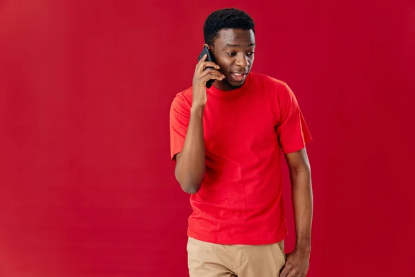 Man av afrikanskt utseende i en röd t-shirt med en telefon i händerna — Stockfoto