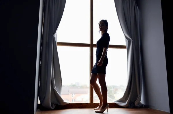 Mulher posando em vestido preto perto da janela silhueta modelo — Fotografia de Stock