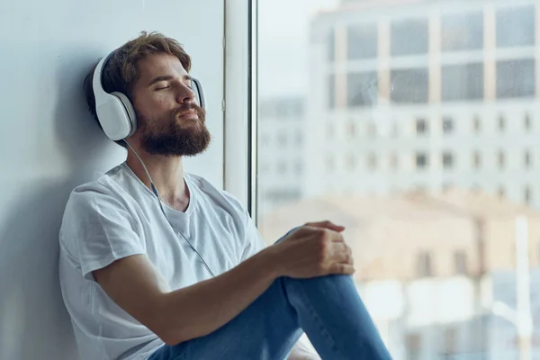 Mężczyzna siedzi na parapecie w słuchawkach w słuchawkach Styl życia — Zdjęcie stockowe