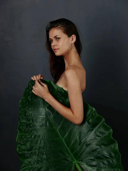 Bonita mujer con el cuerpo desnudo está cubierto por una gran hoja verde fondo oscuro — Foto de Stock