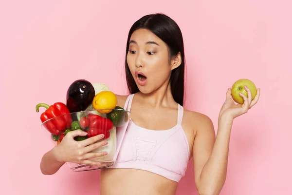Mujer asiática con comestibles en la mano sobre fondo rosa mirada sorprendida —  Fotos de Stock