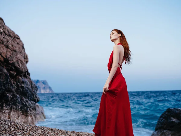 Γυναίκα με κόκκινο φόρεμα που θέτουν βραχώδη βουνά ωκεανούς — Φωτογραφία Αρχείου