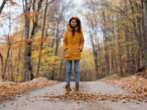 Frau in gelber Jacke im Wald unterwegs Herbstlaub — Stockfoto