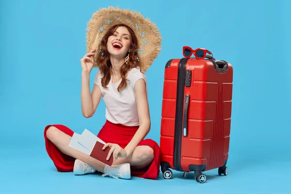 모자를 쓴 쾌활 한 여자가 여행 가방 목적지와 함께 바닥에 앉아 있습니다 — 스톡 사진