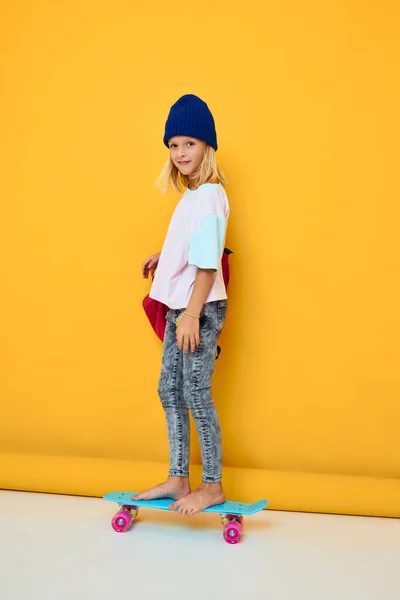 Skolflicka rider en skateboard med en röd ryggsäck isolerad bakgrund — Stockfoto