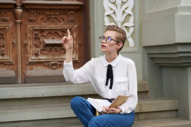 Elinde kitapla dışarıda Yaşam Tarzı okuyan bir öğrenci.