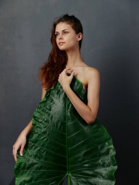 Yeşil yapraklı kadın çıplak vücudu örtüyor.