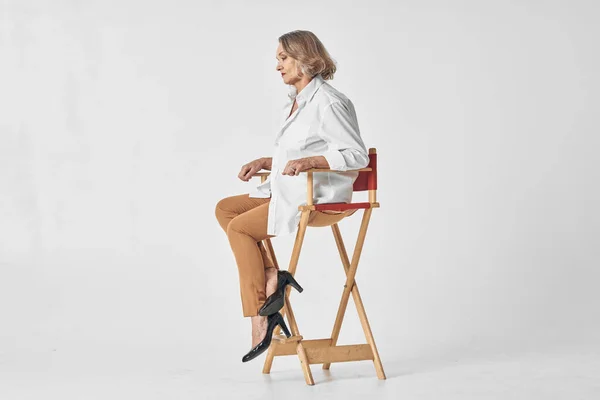 Mujer anciana en camisa blanca se sienta en una silla labios rojos fondo aislado — Foto de Stock