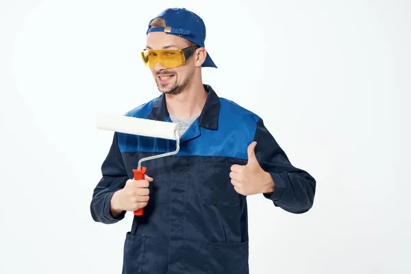 Un homme en uniforme de travail un rouleau pour peindre les murs dans ses mains réparation de décoration — Photo