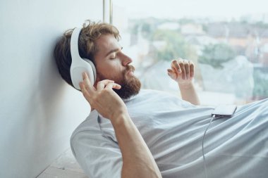 Pencerenin yanında sakallı bir adam var. Kulaklık takıyor. 