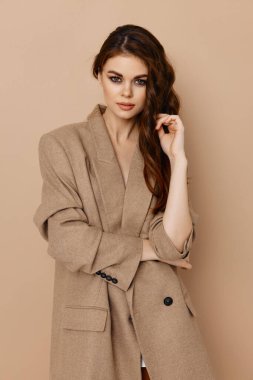 Bej ceketli çekici bir kadın. El kol hareketleri yapıyor ve saçları dökülüyor.