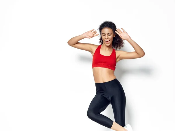 Een vrouw in een kort T-shirt en legging houdt haar handen achter haar hoofd op een lichte achtergrond — Stockfoto