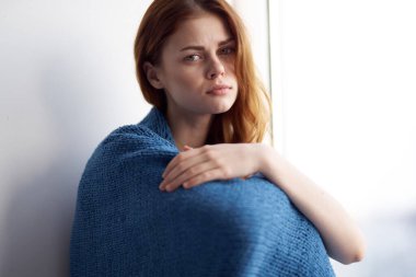 Pencerenin yanında oturan mavi ekose elbiseli kadın. 