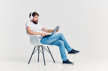 Genç adam elinde dizüstü bilgisayarla sandalyede oturuyor. 