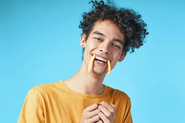 Uomo con i capelli ricci patatine fritte in bocca divertente spuntino sfondo blu — Foto Stock