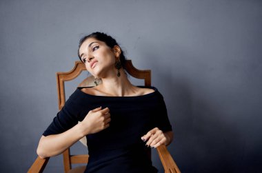 Sandalyenin yanındaki siyah elbiseli güzel kadın lüks moda izole edilmiş arka plan.