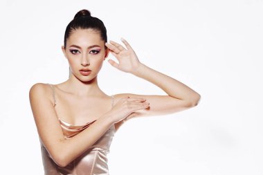 Şeftali rengi saten elbise giymiş şık bir kadın model narin el hareketleriyle poz veriyor. Temiz beyaz arka plan, güzellik, cazibe ve zarafete odaklanan yaratıcı moda havasını artırır..
