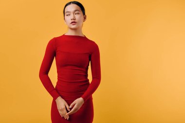 Siyah saçlı, dar kırmızı elbiseli, parlak sarı arka planda duran, sakin gözlü, yumuşak doğal ışık ve temiz arka planda duran genç bir kadın..