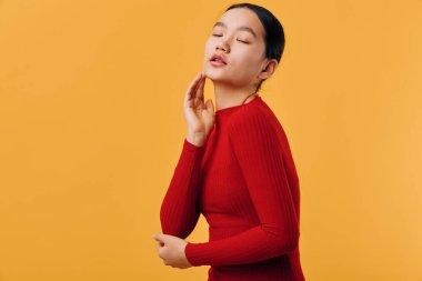 Kırmızı kazaklı sakin bir kadının portresi gözleri kapalı ve yüzüne dokunuyor. Güzellik, moda ve dingin duygu fikri için turuncu arka planlı stüdyo çekimi.