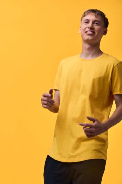 Sarı tişört giyen neşeli bir adam sarı bir arka planda duruyor, kapalı stüdyo ışıkları gündelik moda ve kendine güvenen titreşimleri vurguluyor, sıcak, güneşli bir ruh hali ve basit bir yaşam tarzı ya da
