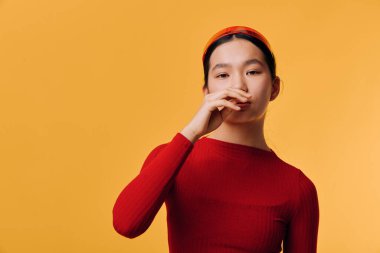 Kırmızı elbiseli ve ağzı turuncu bantlı bir kadın portresi. Stüdyo ortamında yumuşak ışıklandırma ve gündelik pozlarla izole edilmiş..