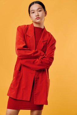 Kırmızı elbiseli ve ceketli genç bir kadın turuncu arka planda kollarını kavuşturmuş poz veriyor. Gösterişli saç stili ve minimum makyajlı modaya uygun giyinen kendine güvenen kadın modelin portresi..